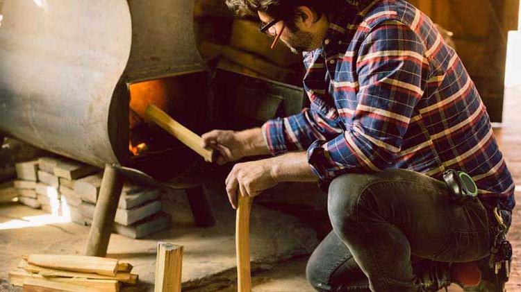 Man placing firewood in a wood stove.