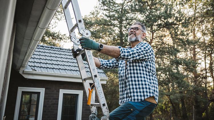 Man climbs a ladder to clear roof of fire-prone debris.