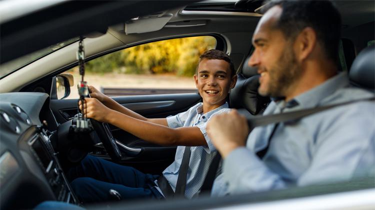 A father putting on his seat belt in his teen son’s first car.